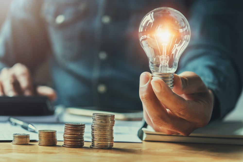 Business,Man,Hand,Holding,Lightbulb,With,Using,Calculator,To,Calculate